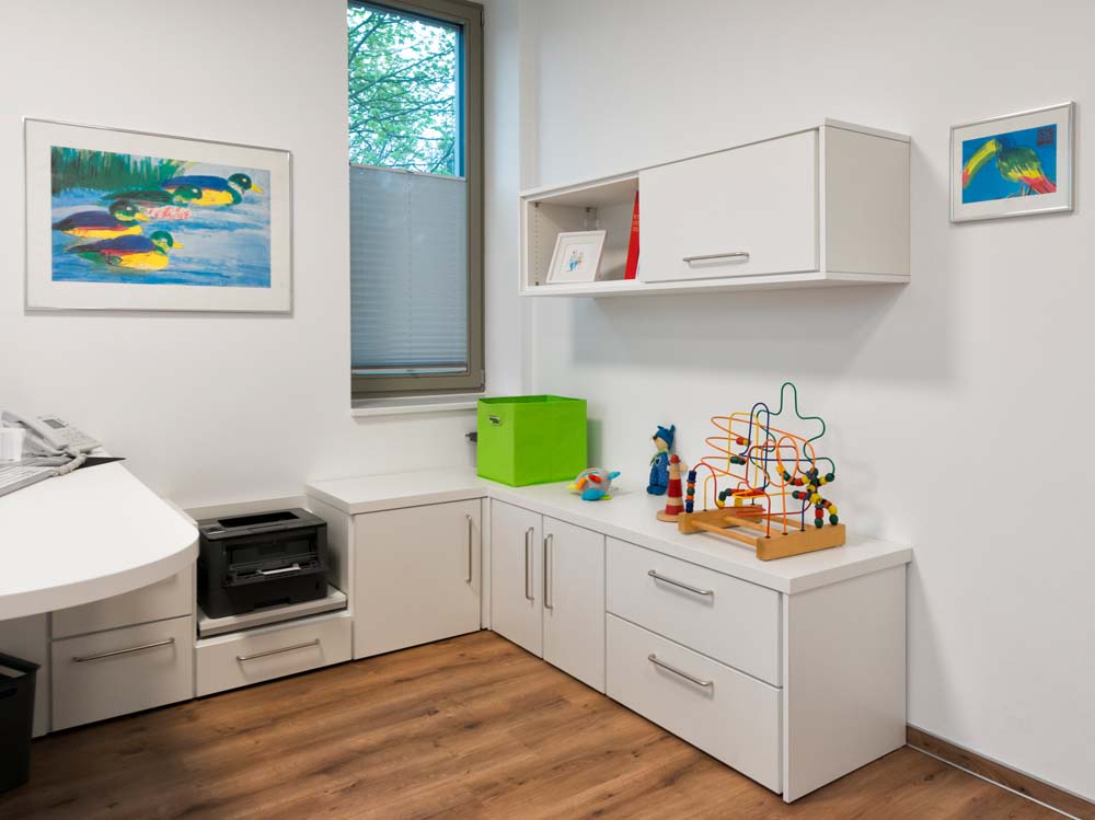 Arztraum mit Tiefschrankwand ums Eck mit integrierter Stellfläche für Drucker und Hochschrank.