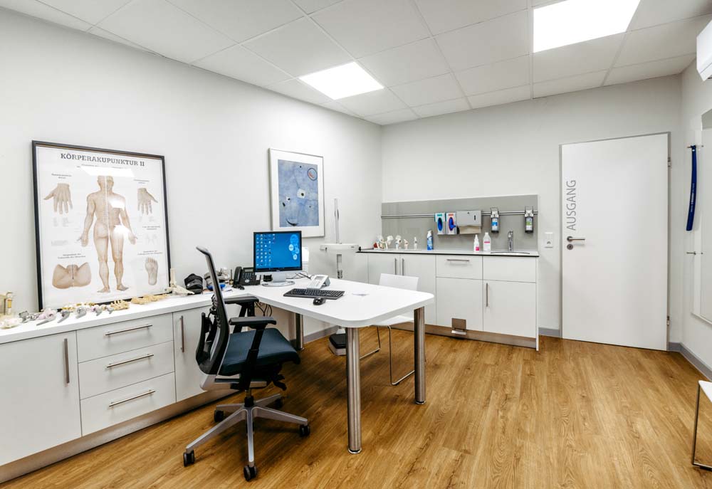 Praxisraum mit Schreibisch und zwei Schrankwänden. Einer mit integrierter Handwaschstation.