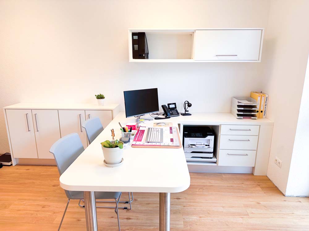 Arztbüro mit weißem Schreibtisch sowie anliegenden Schränken und Schubladensystemen.